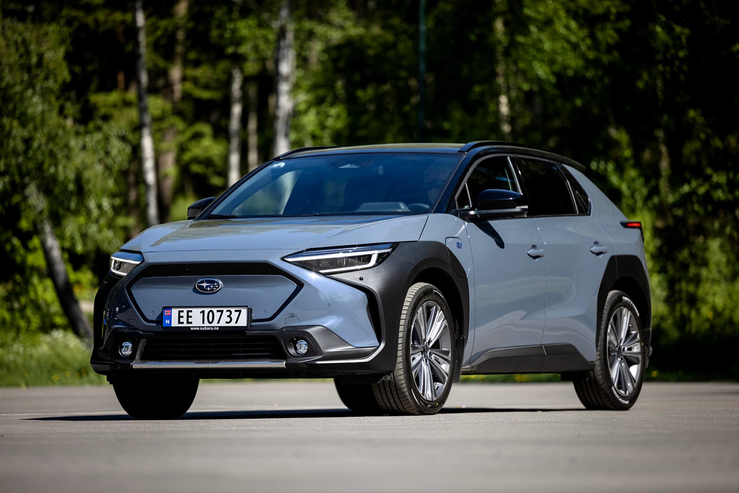 Grå og svart Subaru Solterra foran grønne trær