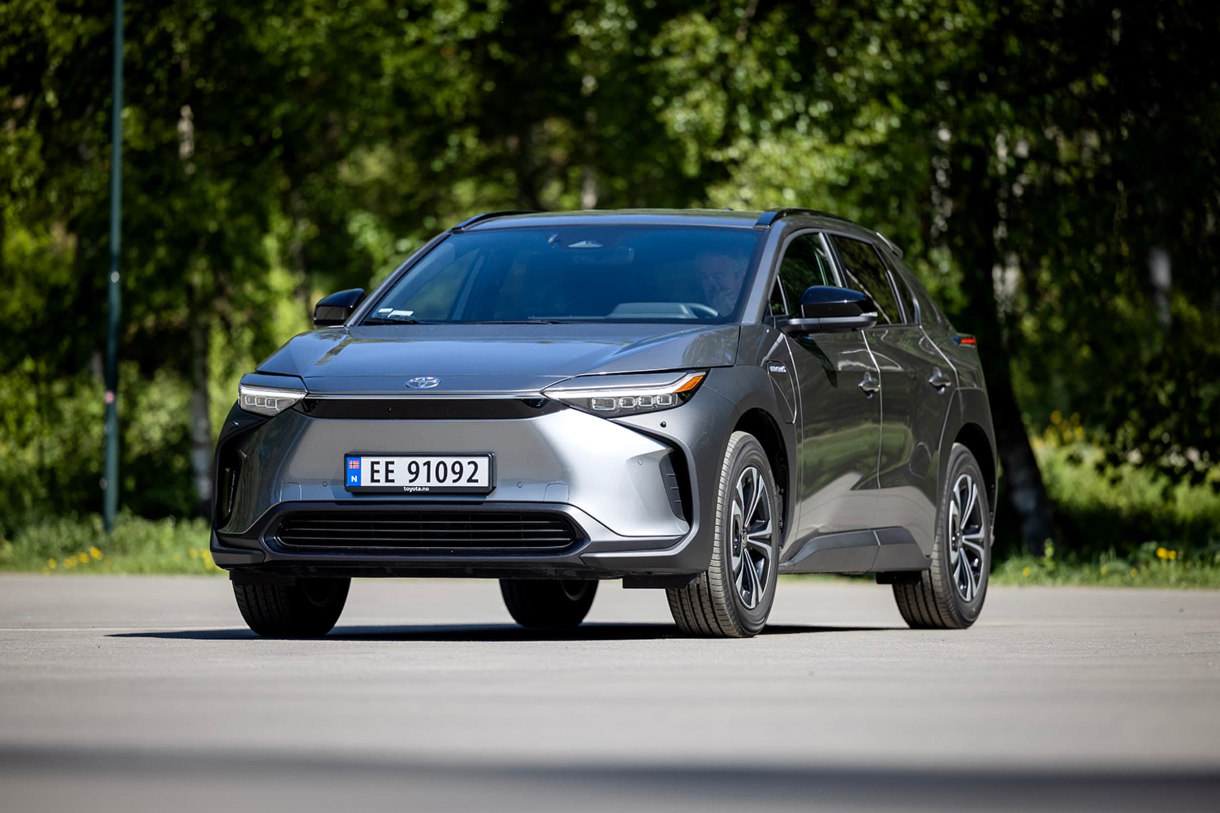 Sølvrgå Toyota BZ4X foran grønne busker